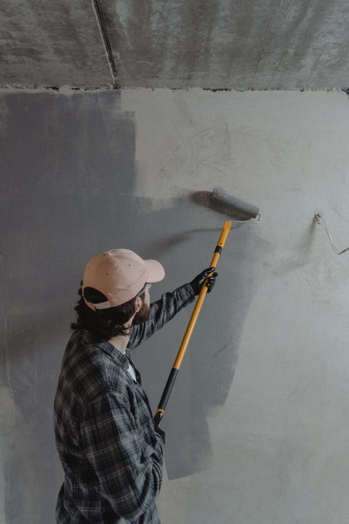 The Art of Drawing Readers In: Your attractive post title goes here A man using a paint roller to apply gray paint on a wall in an unfinished room.