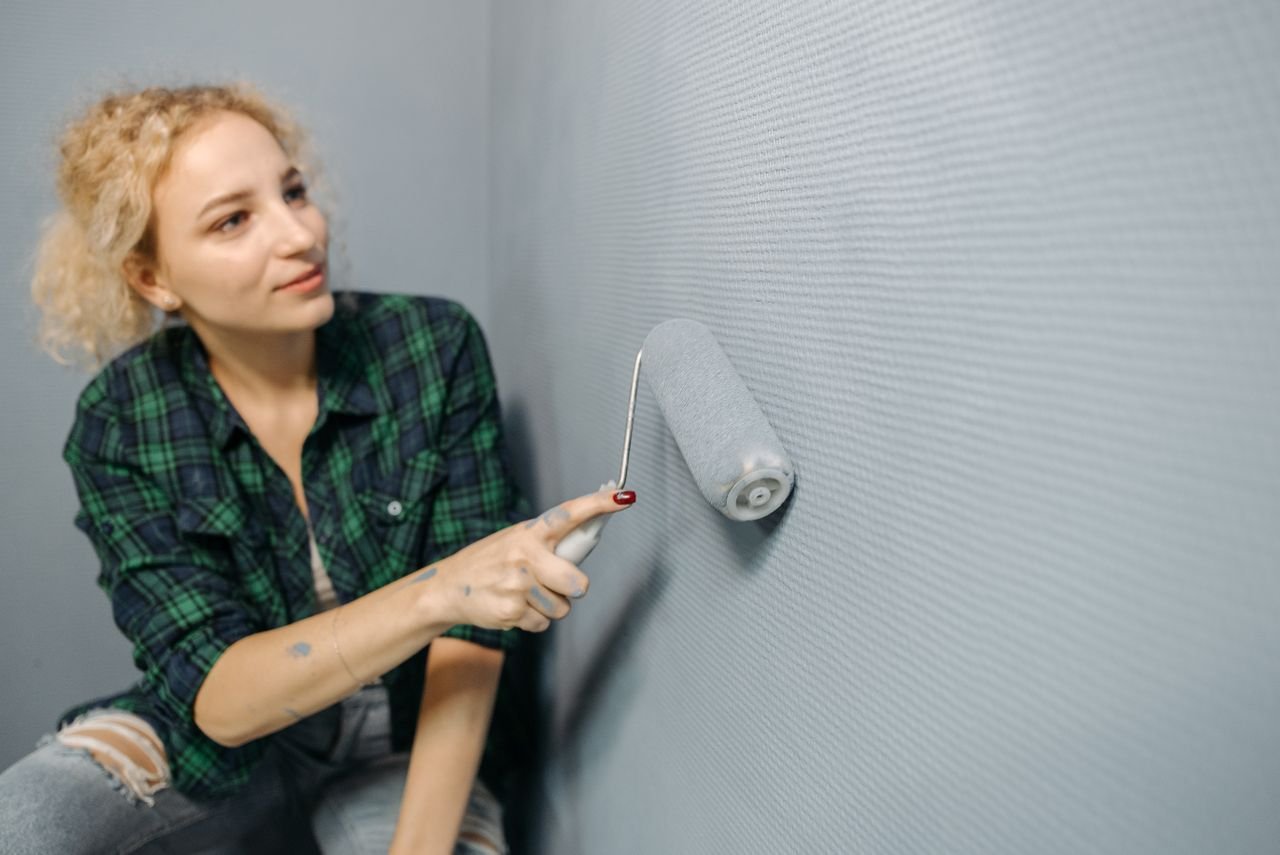 A woman uses a paint roller to apply paint on a wall, part of a home renovation project.